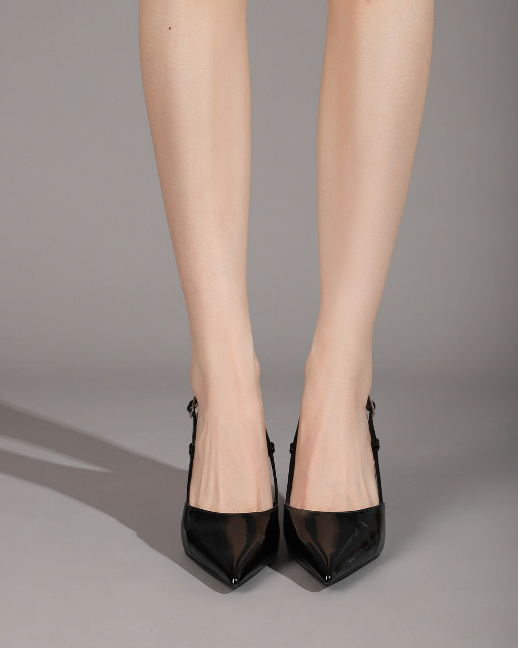 Black patent pointed-toe slingback pumps on foot 1