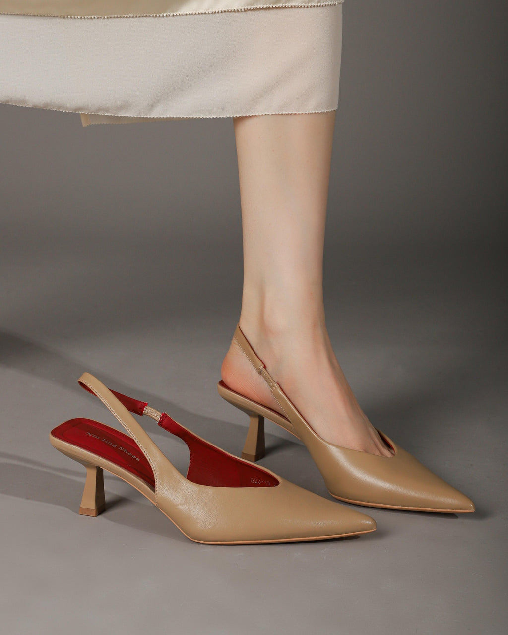 Khaki pointed-toe slingback heel modeled with one shoe alongside